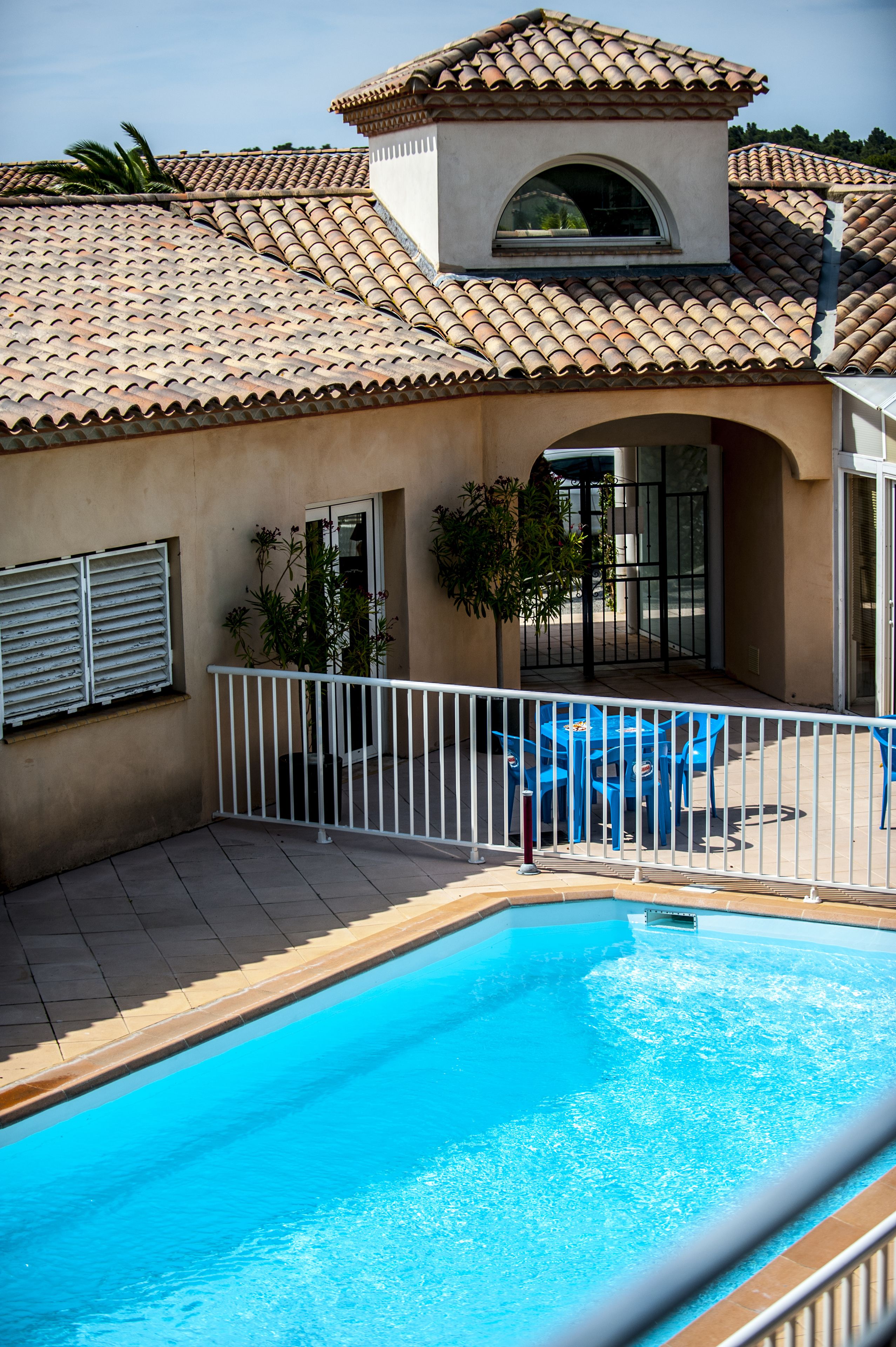 Una piscina con techo de azulejos, barandilla blanca y una pequeña zona de estar con sillas azules.