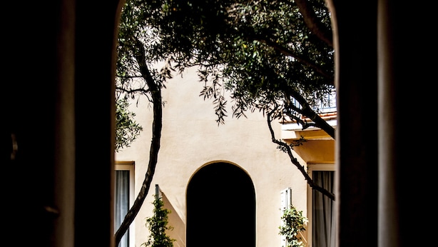 An arched corridor with a tiled floor leading to a building with a large arched doorway. - Hôtel Leukos (Leucate)