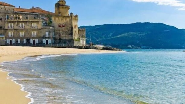 Un edificio costero con una torre, ubicado cerca de una playa con aguas azul turquesa.