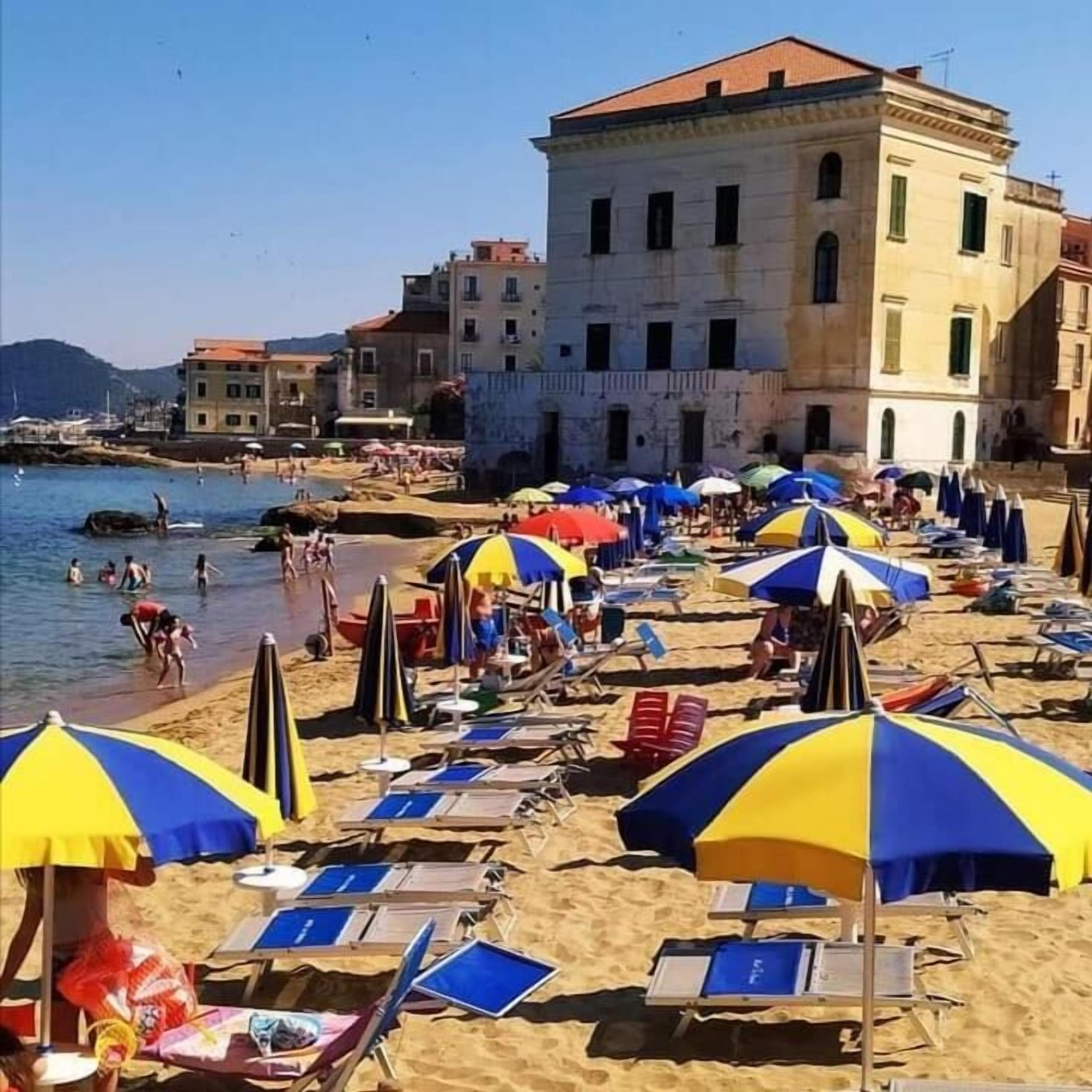 A beach with rows of sun loungers and umbrellas, a building in the background, and people in the water.