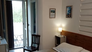 Un dormitorio con cama, una silla, un escritorio y una lámpara. Hay una ventana y una puerta que da a un área exterior.