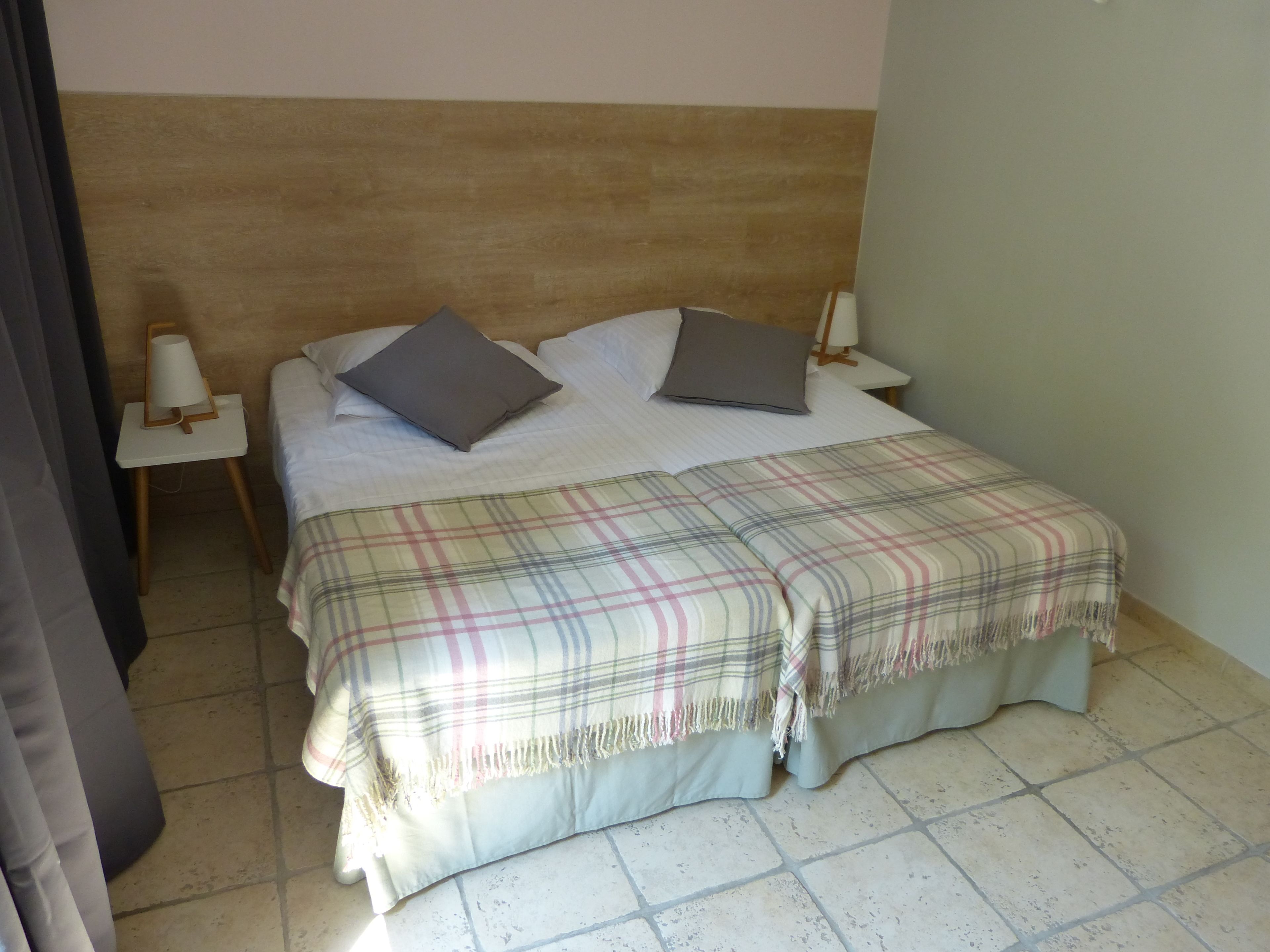 Un lit bien fait, avec une couverture à carreaux, deux oreillers et une lampe de chevet posée sur une petite table.