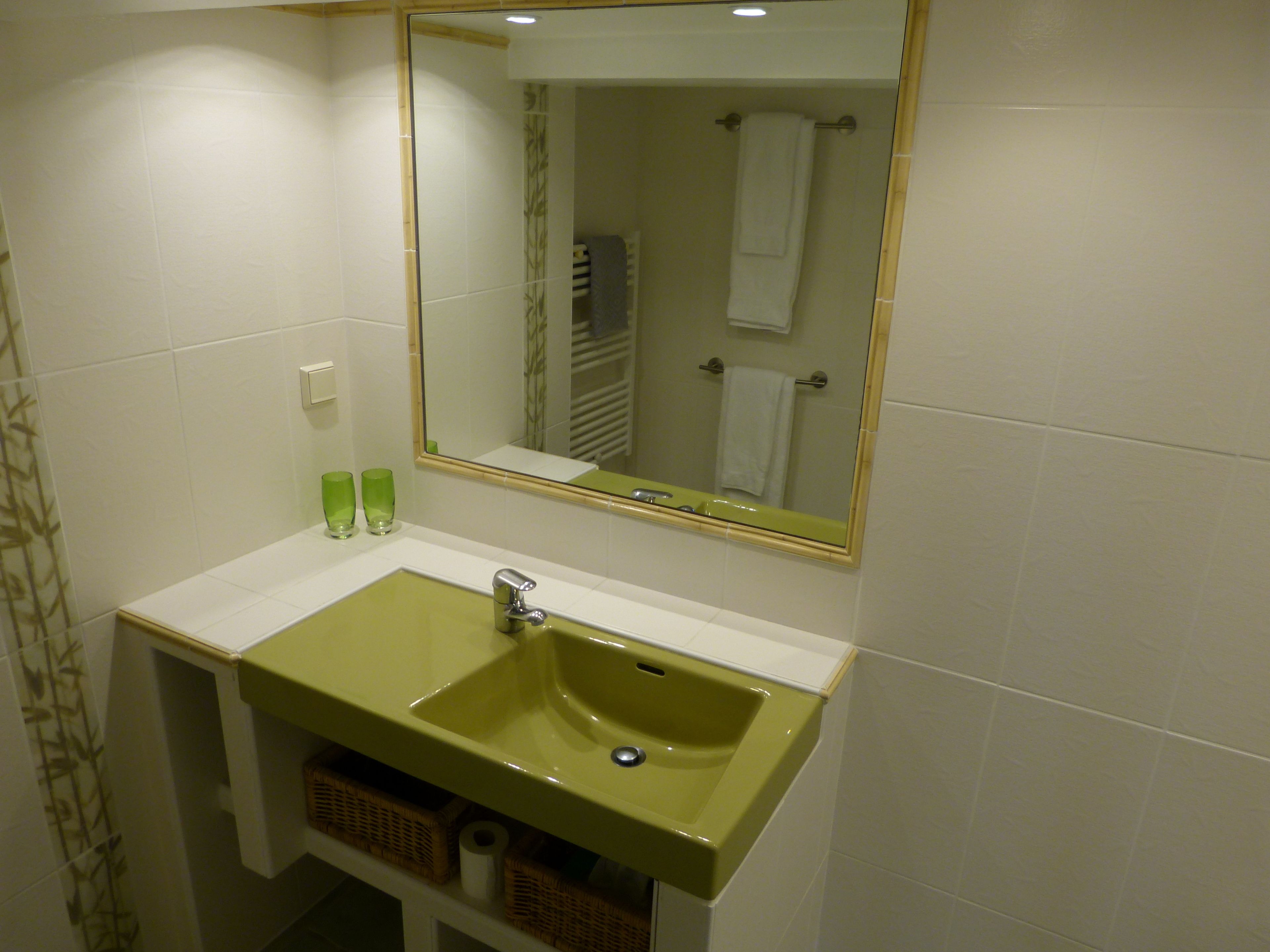 Een badkamer met een groen wastafel, een spiegel en twee groene glazen op het aanrecht.