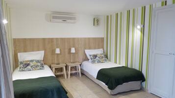 A hotel room with two beds, a wooden headboard, a wall-mounted air conditioner, and striped wallpaper.