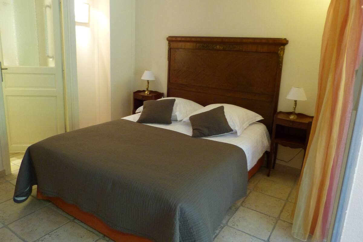 A neatly made bed with a wooden headboard, two bedside tables with lamps, and a door to the left.