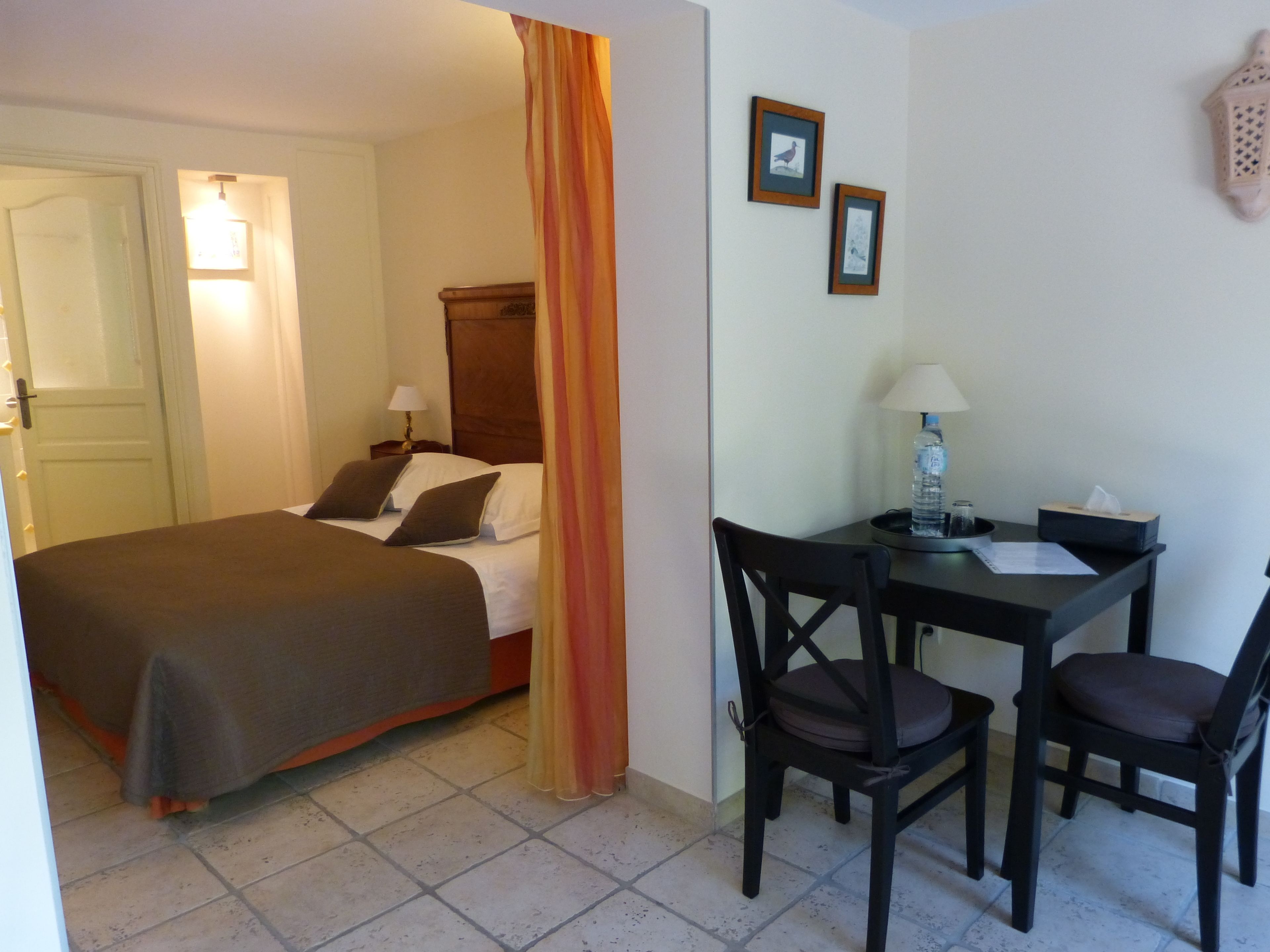 Ein Hotelzimmer mit Bett, Schreibtisch, Stuhl, Lampe und einer Wasserflasche.