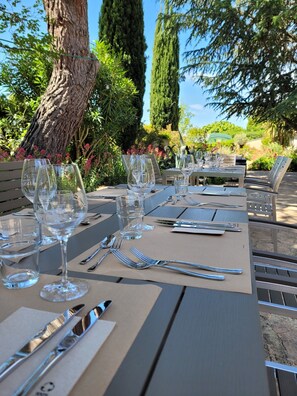 Un área de comedor al aire libre con mesas dispuestas para una comida, rodeada de follaje y árboles.