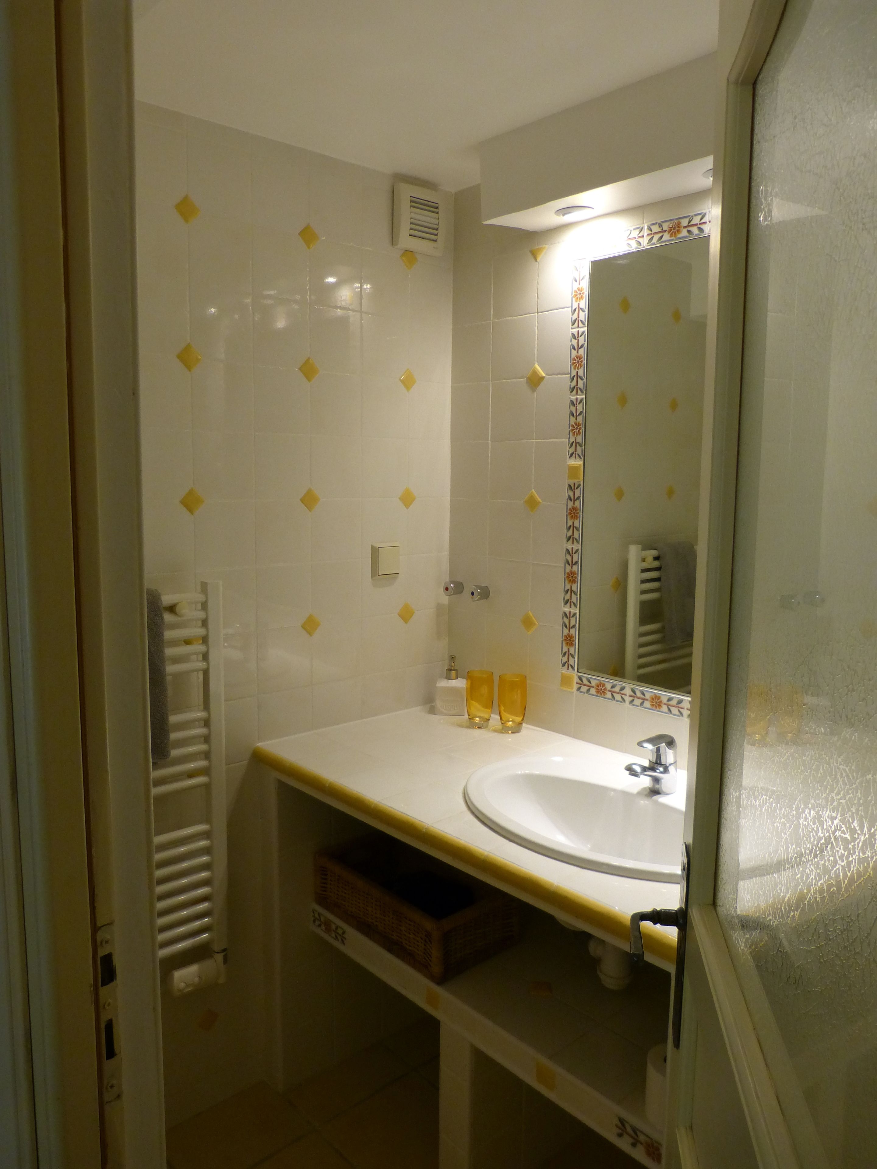 A bathroom with a white sink, yellow diamond-patterned tiles, a mirror with a decorative frame, and a towel rack.