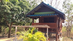 A wooden cabin with a balcony, surrounded by trees and a small palm plant in the foreground. - Romsiri Resort (Sung Noen)