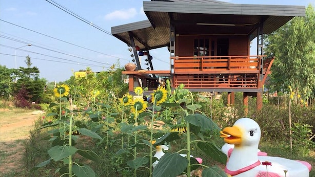 A rustic wooden cabin with a balcony, surrounded by a garden with sunflowers. - Romsiri Resort (Sung Noen)