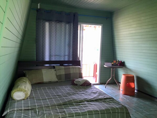 Una habitación pequeña y acogedora con cama, ventana con cortinas, una mesita con fruta y un taburete.
