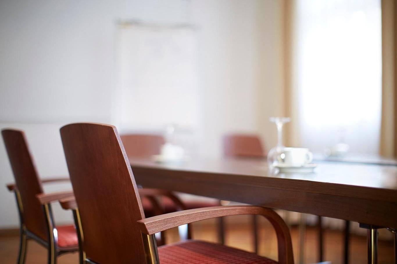 Ein Konferenzraum mit einem langen Holztisch, roten Sitzmöbeln und einer Tafel im Hintergrund.