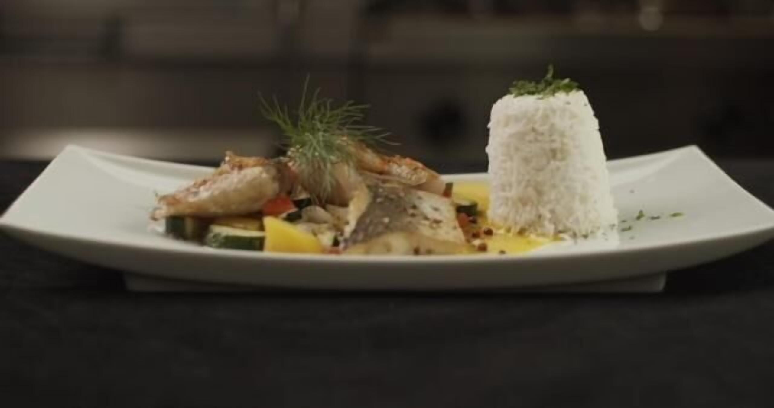 A plate with a fish dish, vegetables, and a mound of white rice.