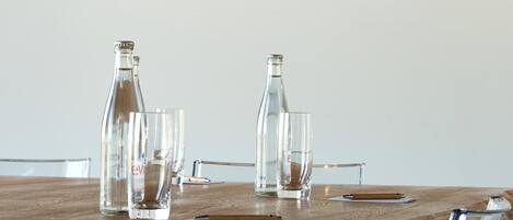Una mesa con dos botellas y dos vasos, con vistas a un paisaje pintoresco con colinas y una masa de agua.