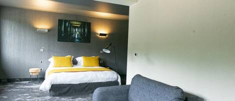 A modern hotel room with a large bed, a gray sofa, and a painting on the wall.
