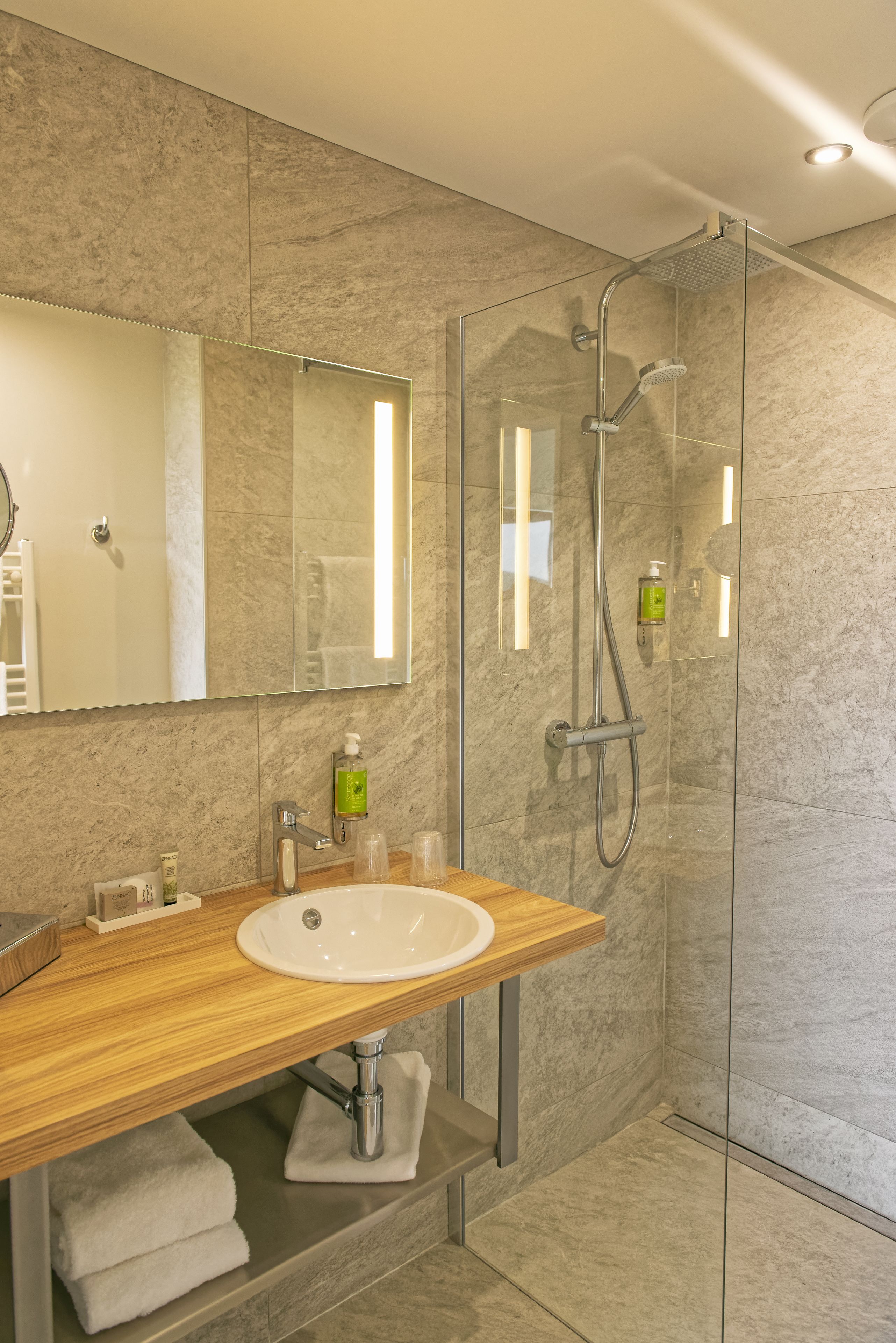 A modern bathroom with a glass-enclosed shower, a wooden vanity, and a large mirror.