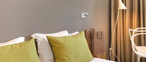 Habitación de hotel con cama, almohadas, lámpara, una silla y un cuadro en la pared.