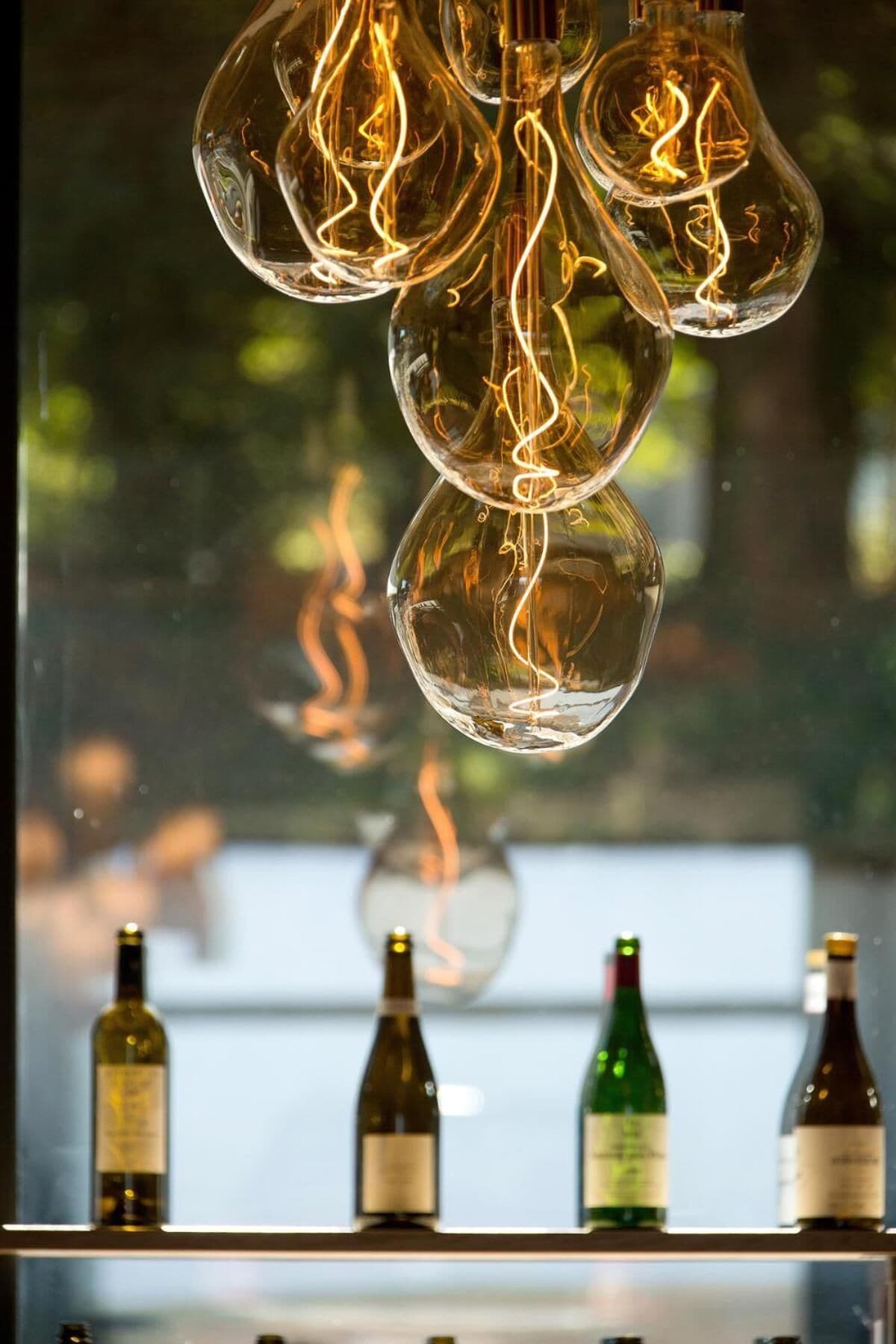 A bar area with hanging light bulbs and bottles of wine on shelves.