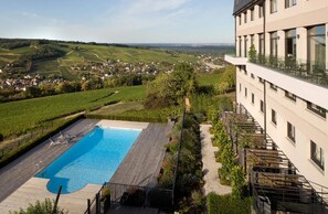 Un hotel con piscina, rodeado de vegetación y viñedos, con vistas a un valle.