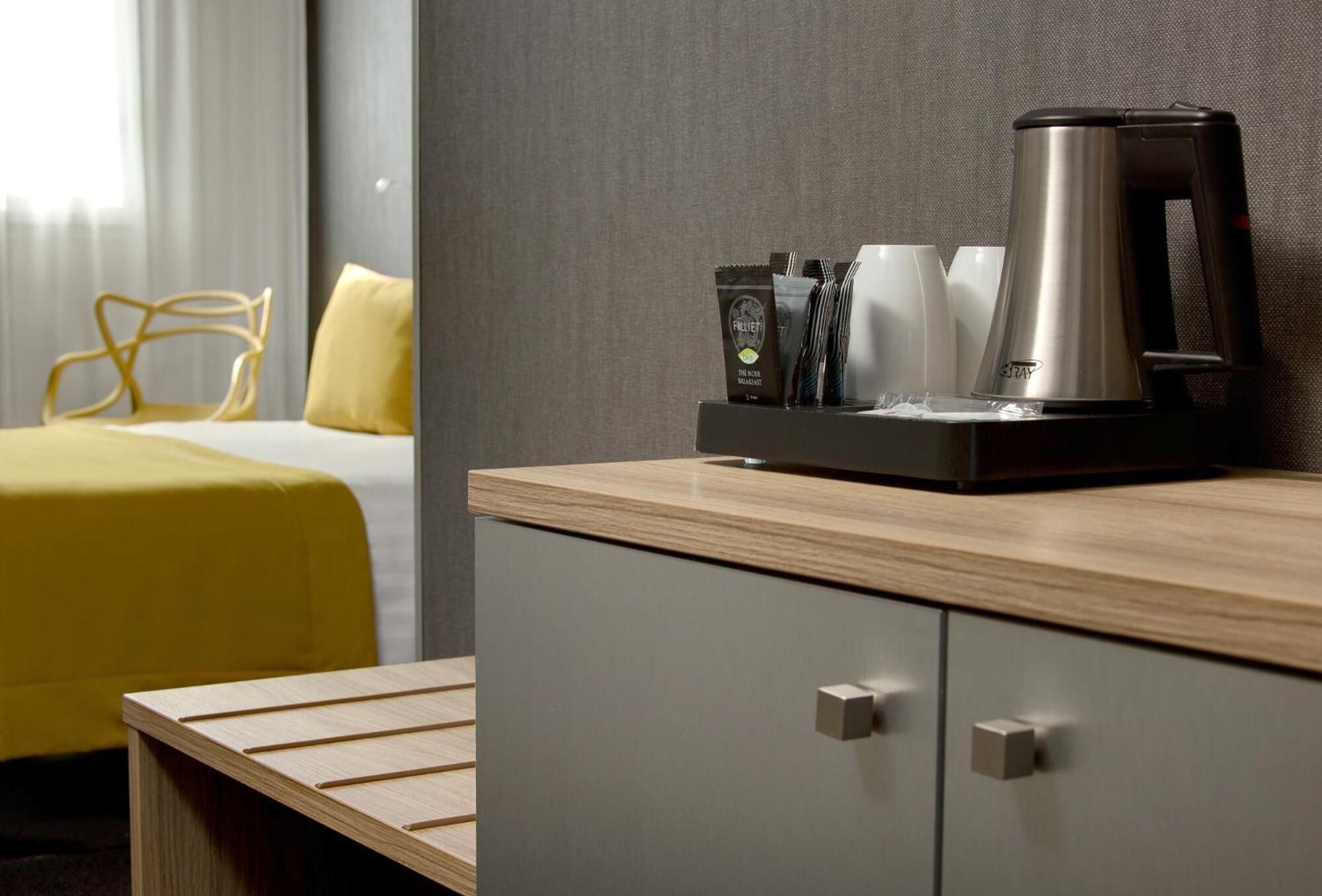 Une chambre d’hôtel avec un lit, une table de chevet en bois, une machine à café et un plateau contenant des dosettes de café et des tasses.