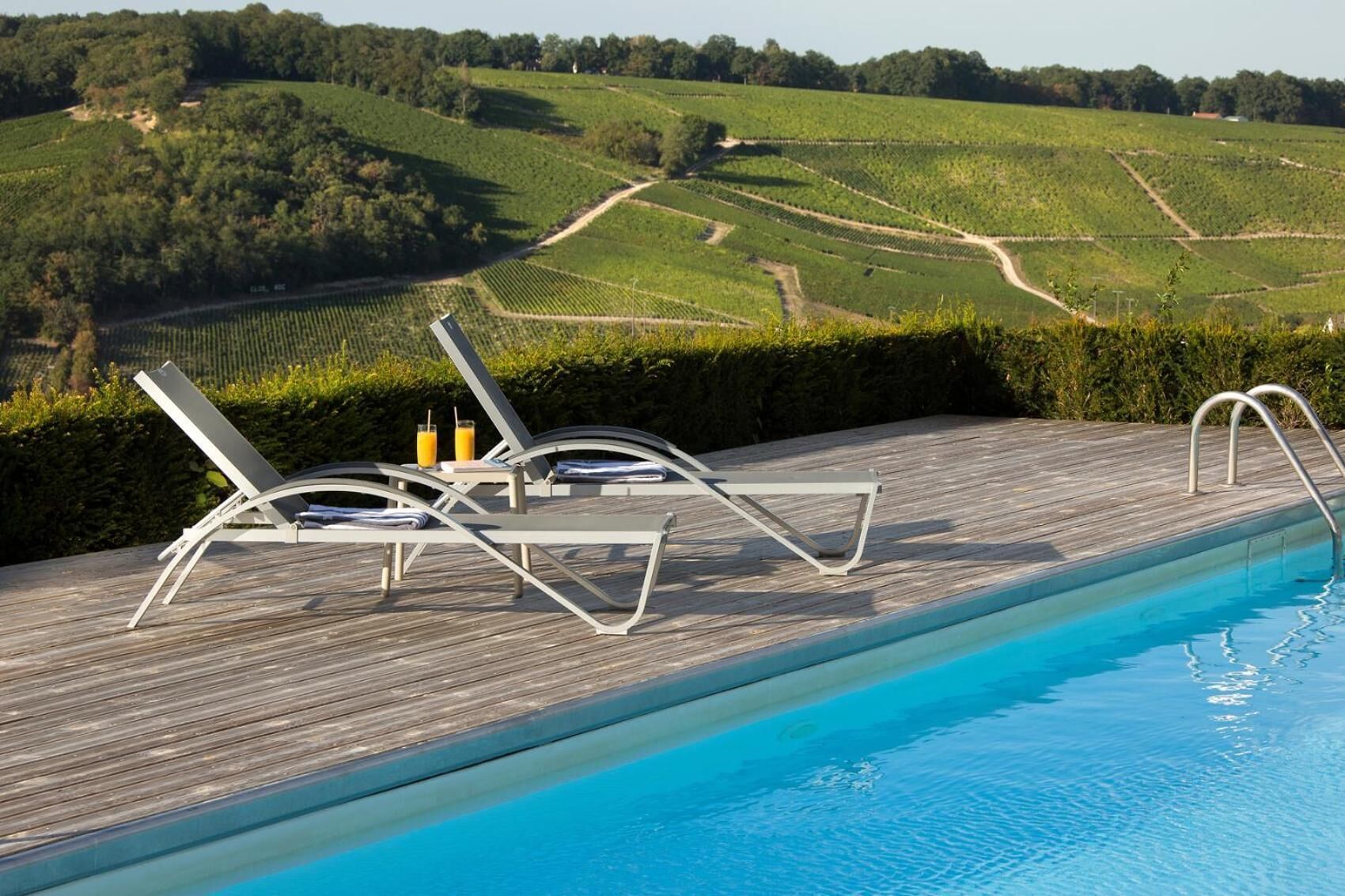 A poolside area with lounge chairs and a view of vineyard rows.