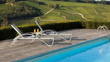 A poolside area with lounge chairs and a view of vineyard rows.