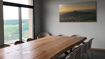 A conference room with a large wooden table, four chairs, and a large window offering a view of a landscape.