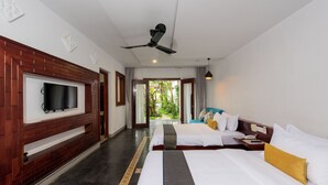 A hotel room with a TV mounted on a wooden panel, two beds with white bedding and yellow pillows, a ceiling fan, and a view of greenery through the door. - Charming Angkor Resort & Spa (Siem Reap)