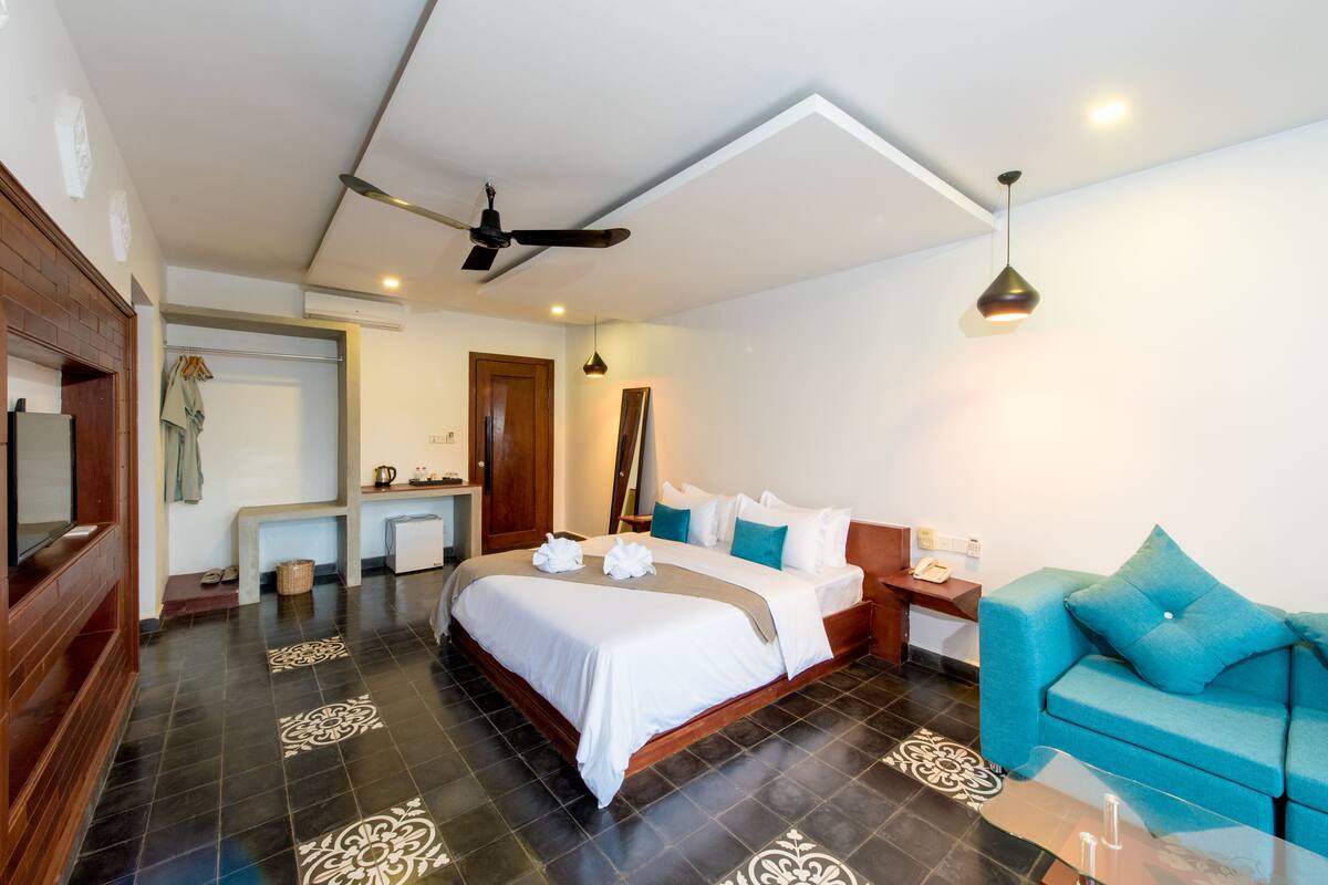 A hotel room with a bed, a desk, a chair, a sofa, a ceiling fan, and a hanging light fixture.
