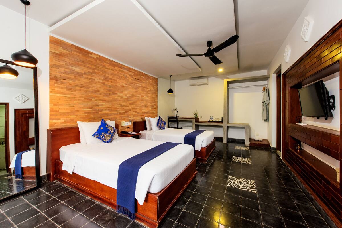 A hotel room with two beds, a wooden headboard, a ceiling fan, and a large mirror.