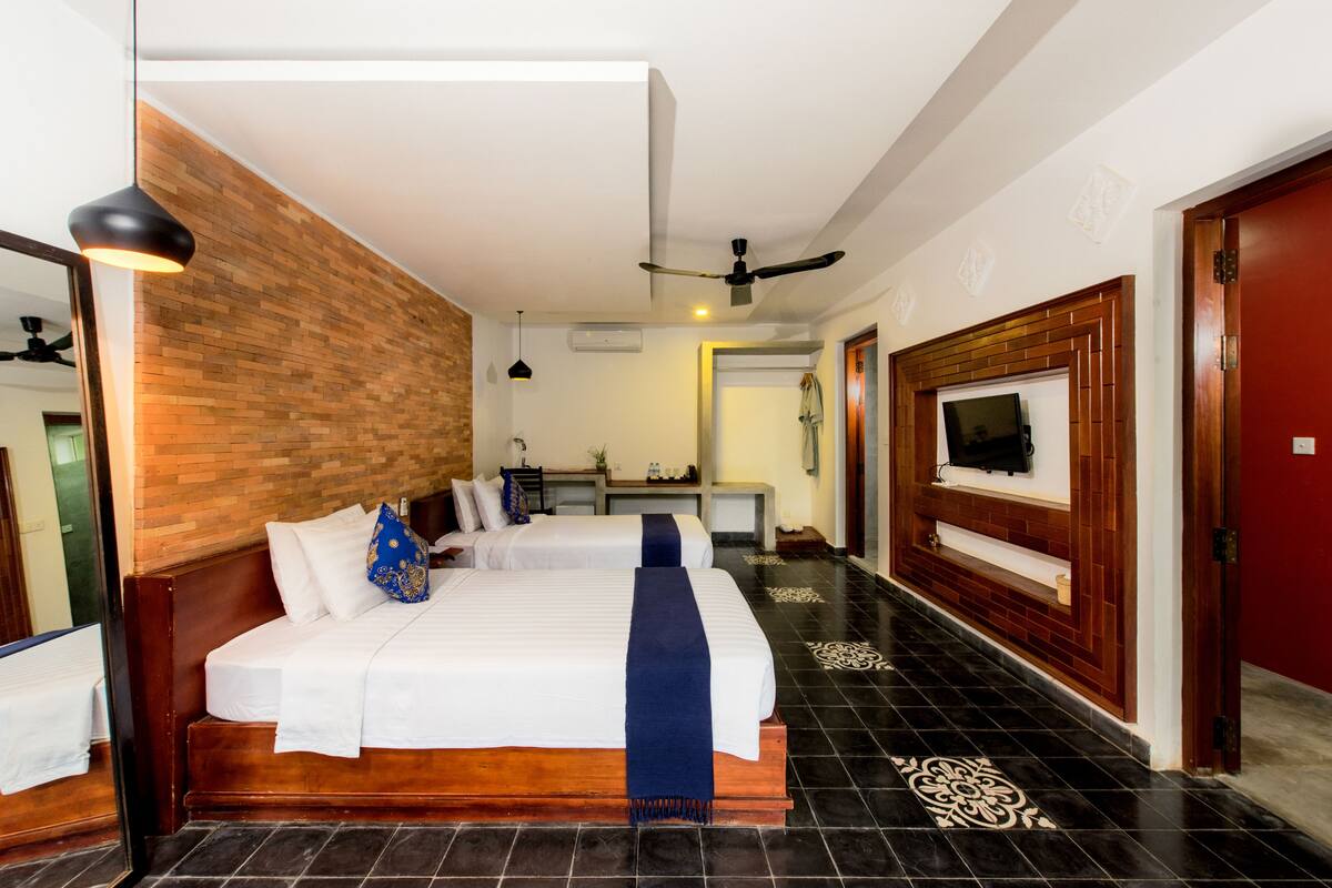 A hotel room with two beds, a TV, a ceiling fan, and a wooden accent wall.