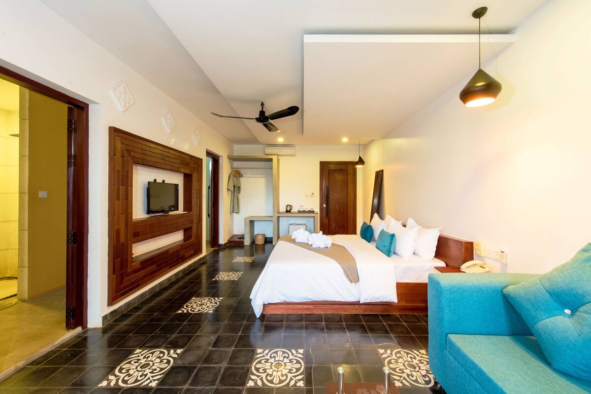 A hotel room with a large bed, a TV mounted on the wall, a ceiling fan, and a modern light fixture.