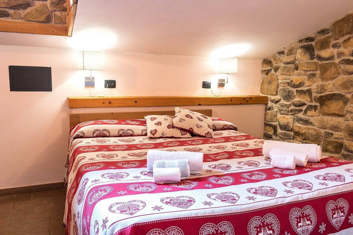 A cozy bedroom with a stone wall, a wooden headboard, and a patterned bedspread.
