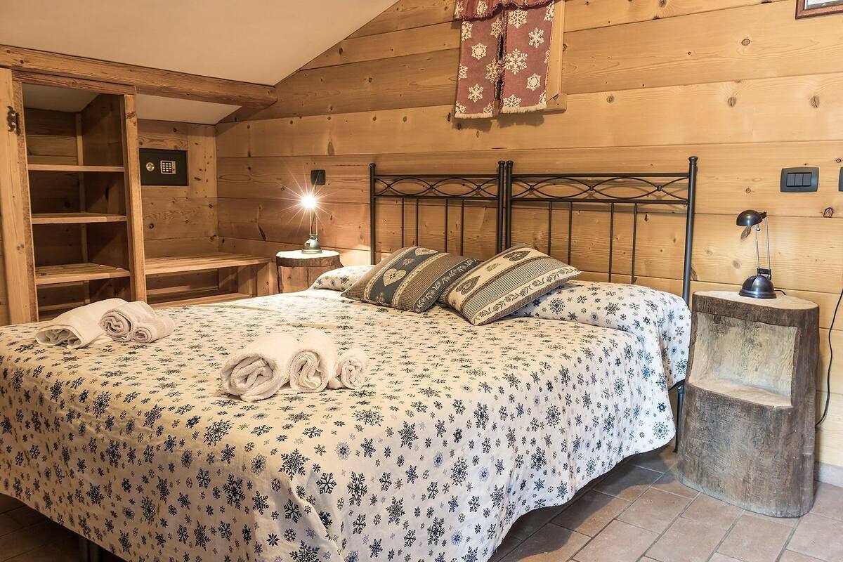 A cozy wooden room with a bed, a bench, a small table, and a nightstand.