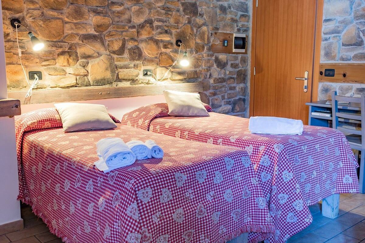 A double bed with checkered bedding, a wooden headboard, and a stone wall.