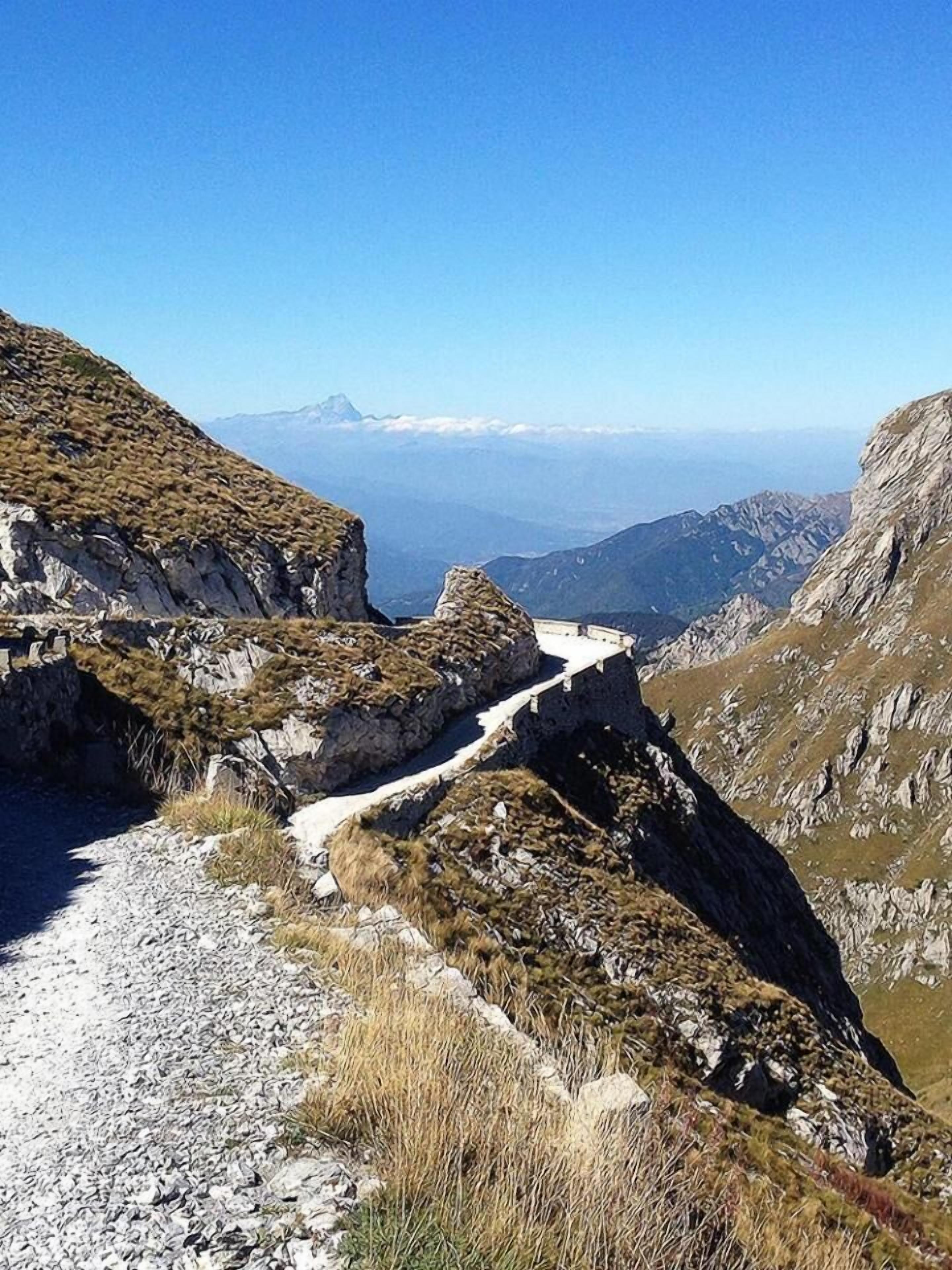 Un sentiero montano impervio con terreno roccioso e vegetazione rada.