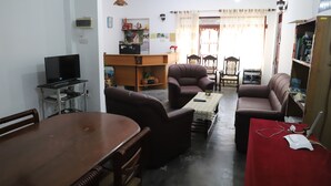 A living room with a wooden dining table, two brown sofas, a TV on a stand, and a bookshelf. - prasad suomi villa (Matara)