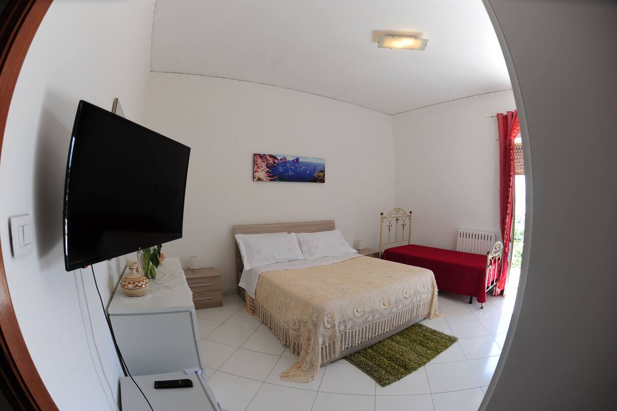 Une chambre à coucher avec un lit, une télévision, un tableau et une table rouge.