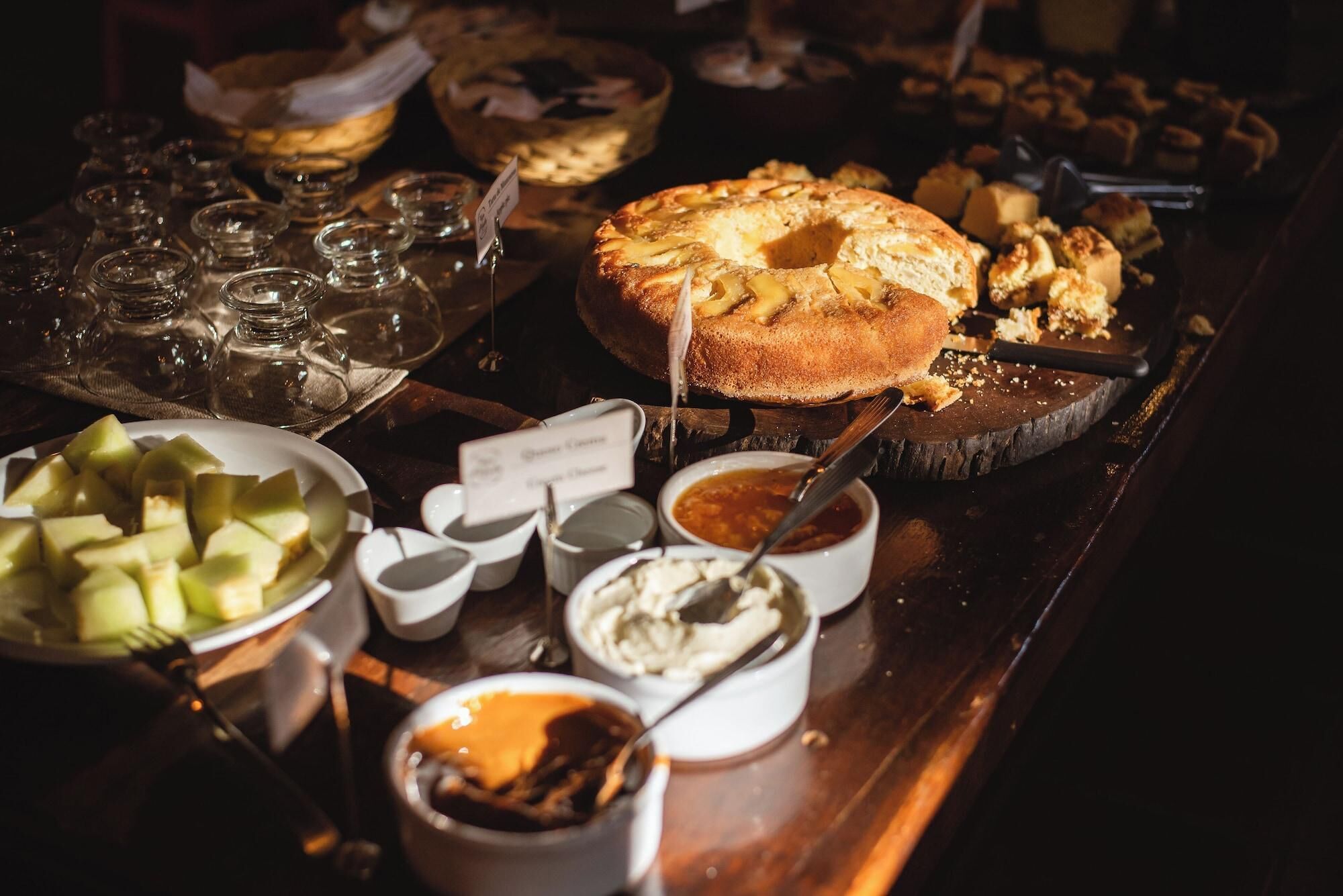 A buffet table with various food items including a large cake, bowls of fruit, and different sauces.