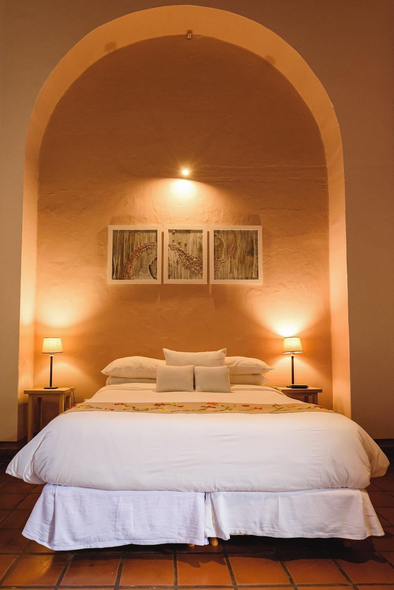 A bedroom with a large bed, two bedside lamps, and three wall-mounted paintings.