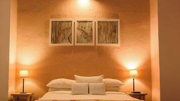 A bedroom with a large bed, two bedside lamps, and three wall-mounted paintings.