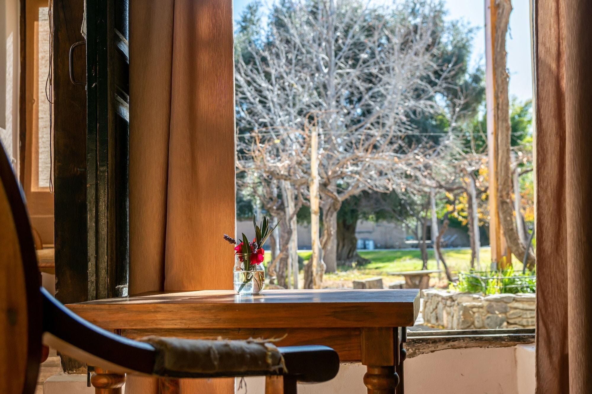A wooden table with a vase of red flowers, a chair, and a view of a tree-lined outdoor area.