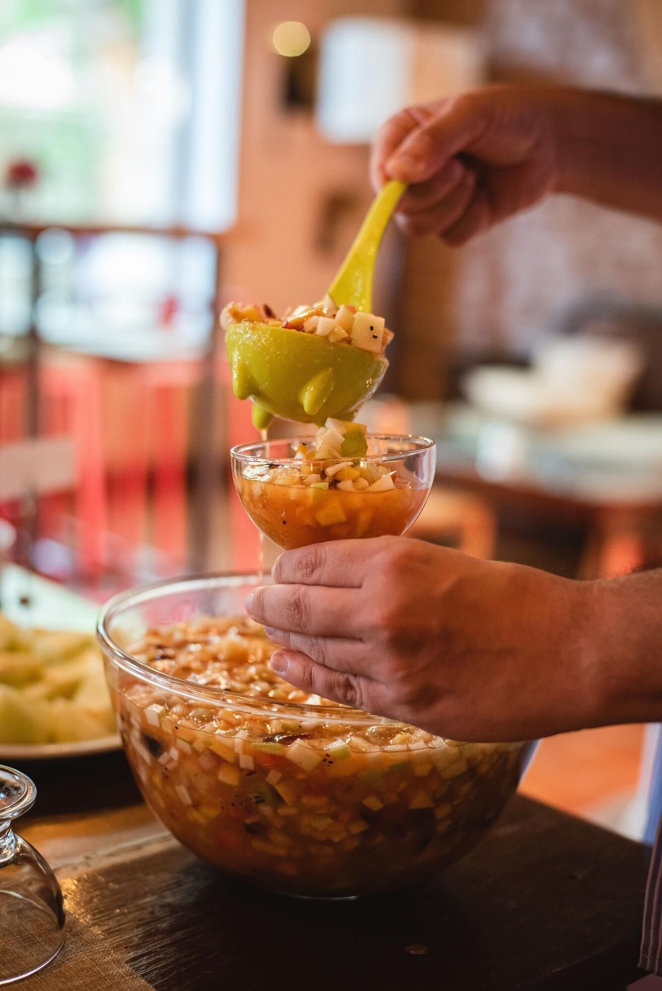 A person serving a dish from a large bowl into a glass bowl using a yellow spoon.