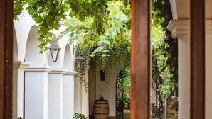 An arched corridor with a cobblestone floor, white columns, and a wooden barrel.