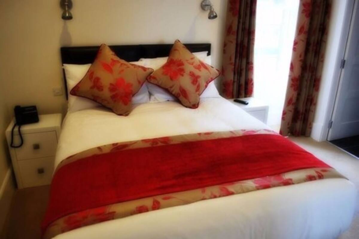 A neatly made bed with a red and beige blanket, two matching pillows, and a bedside table with a lamp.