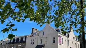 A historic building with a prominent corner entrance, a small adjacent structure, and a clear blue sky. - The Aberlour Hotel (Aberlour)