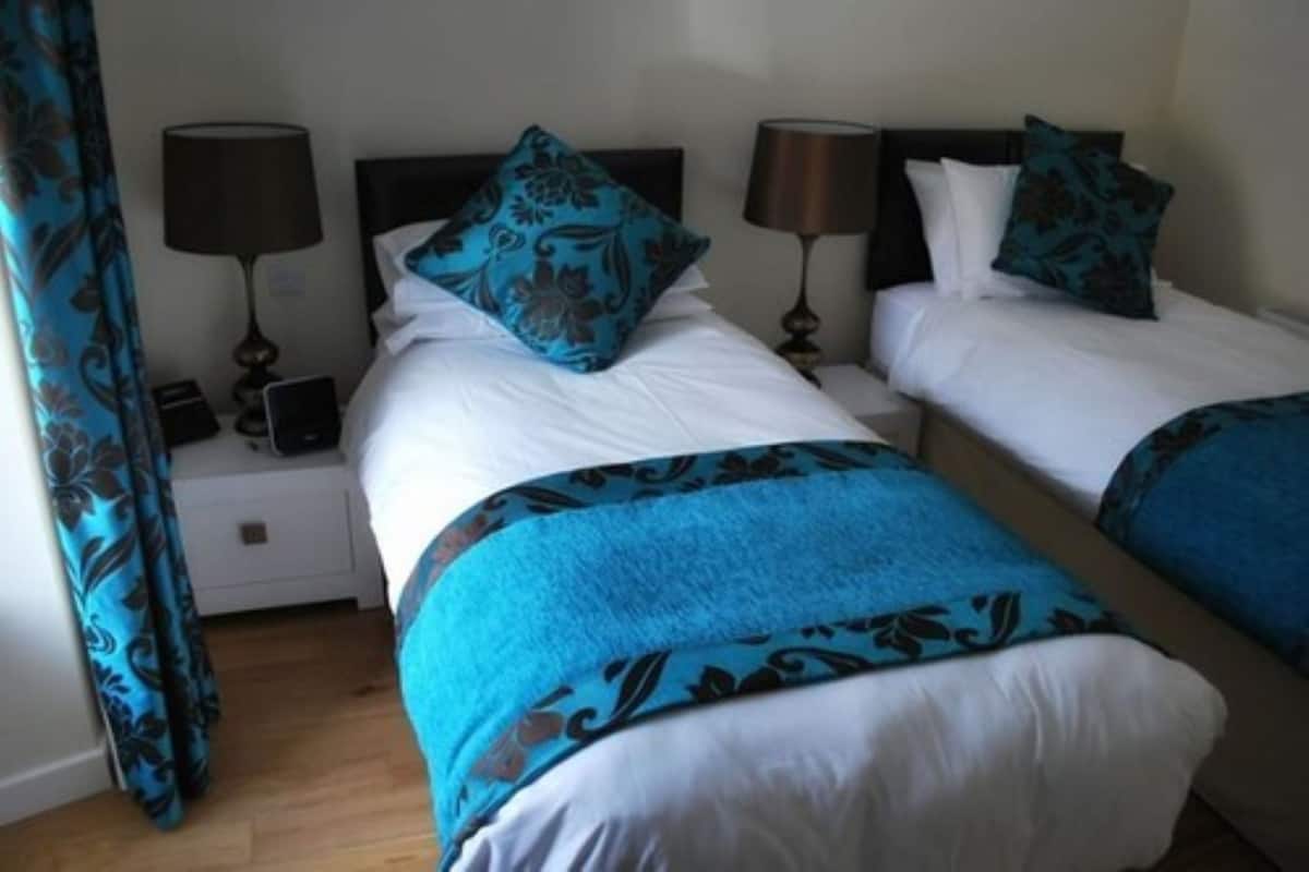 A hotel room with two beds, each with a blue and black patterned bedspread, white linens, and matching lamps on nightstands.