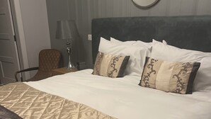 A neatly made bed with a patterned bedspread, a round mirror on the wall, and a chair with a lamp beside the bed. - The Aberlour Hotel (Aberlour)