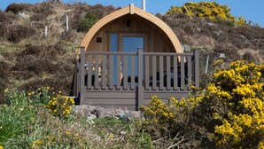 A small wooden cabin with a curved roof and a balcony, surrounded by natural vegetation and hills. - Suil Na Mara (Lochinver)