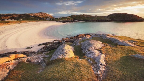 A coastal landscape with a sandy beach, rocky outcrops, and a small settlement in the distance. - Suil Na Mara (Lochinver)